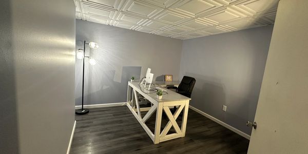 Minimalist home office with a modern desk, chair, and lamp on dark wood flooring.