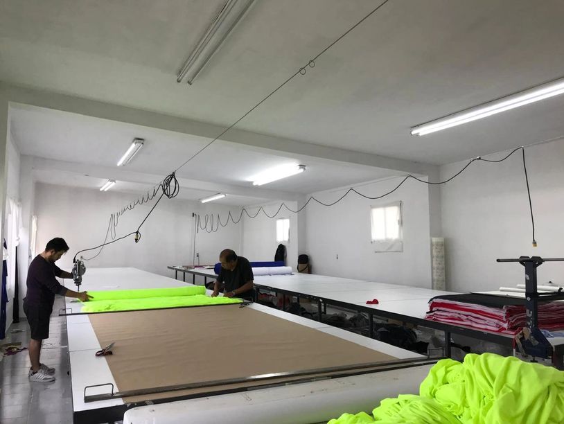 Two men working with bright neon fabric in a spacious workshop.