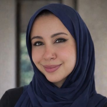 A woman wearing a navy blue hijab smiling gently.