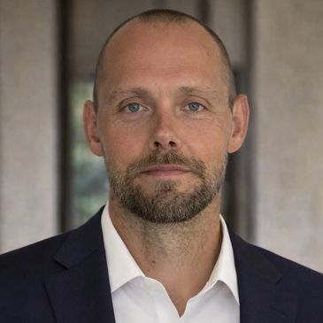 Portrait of a serious man in a suit with a beard and shaved head.