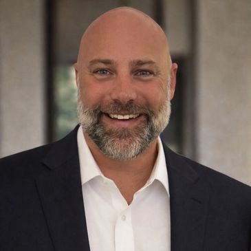 Smiling bald man with a beard in a suit jacket and white shirt.