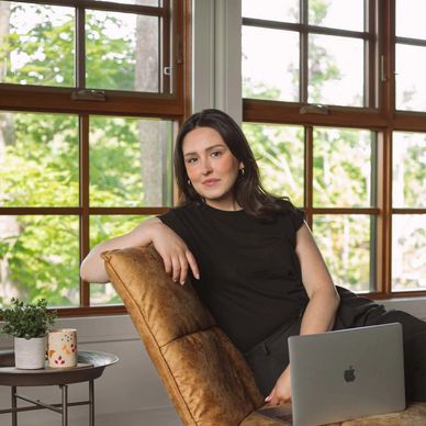 Woman in black dress relaxing on a chair with a laptop.