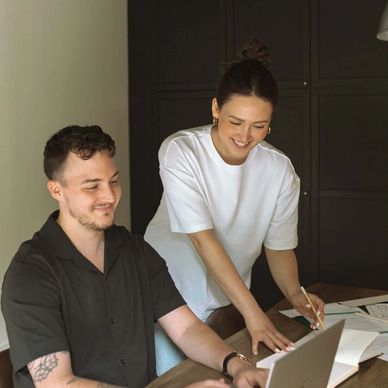 Two colleagues happily working together on a laptop at a desk.