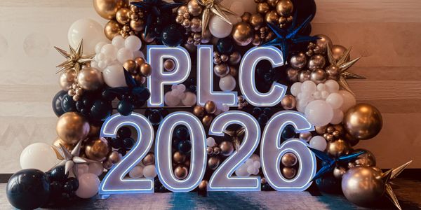 Illuminated letters and numbers "PLC 2026" surrounded by black, white, and gold balloons.