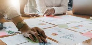A picture of sales charts on a table with two people reviewing them. The persons cannot be seen.
