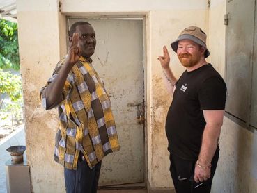 Two men standing by a door, raising their right hands.