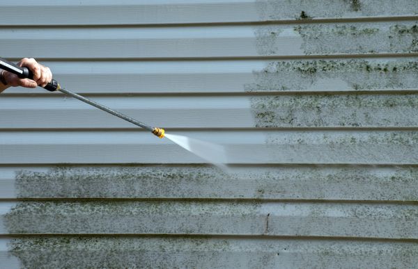 This image shows a man pressure washing a paved patio or walkway in front of a house.