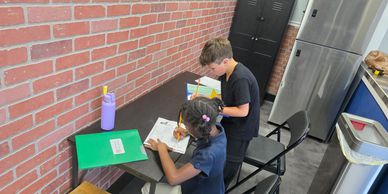 Two children doing homework at a brick wall desk.