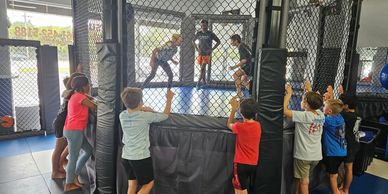 Children watching a martial arts demonstration inside a gym.