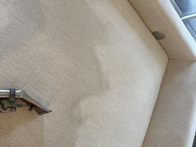 Cleaning a beige fabric sofa with a steam or carpet cleaning tool.