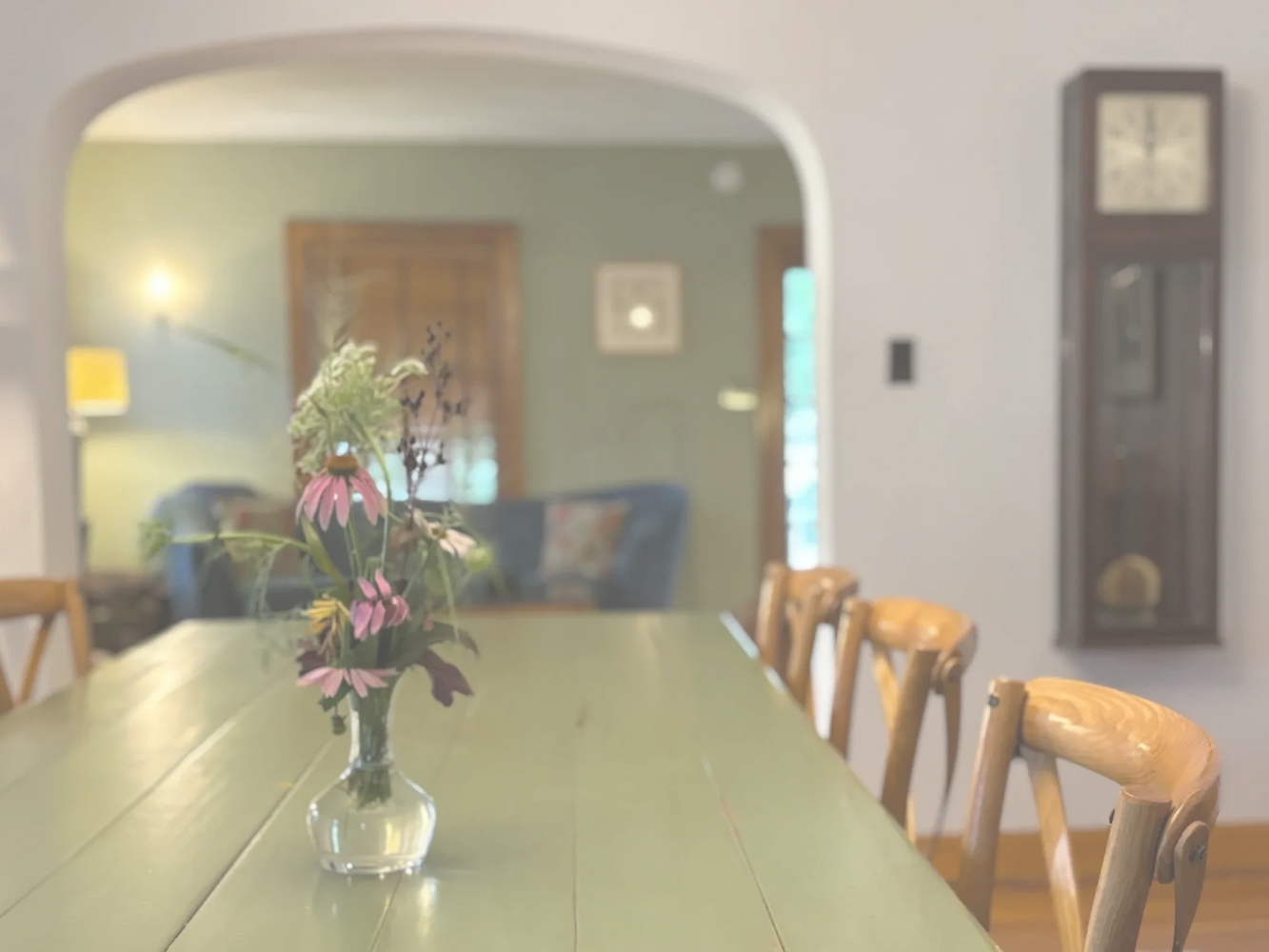 Wildflowers in a vase on a rustic dining table with wooden chairs.