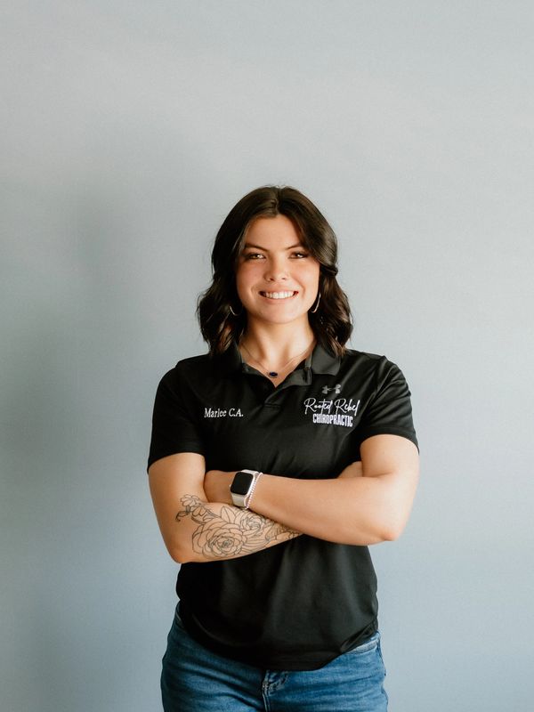 Confident woman with tattooed arm in black chiropractic polo shirt smiles with arms crossed.