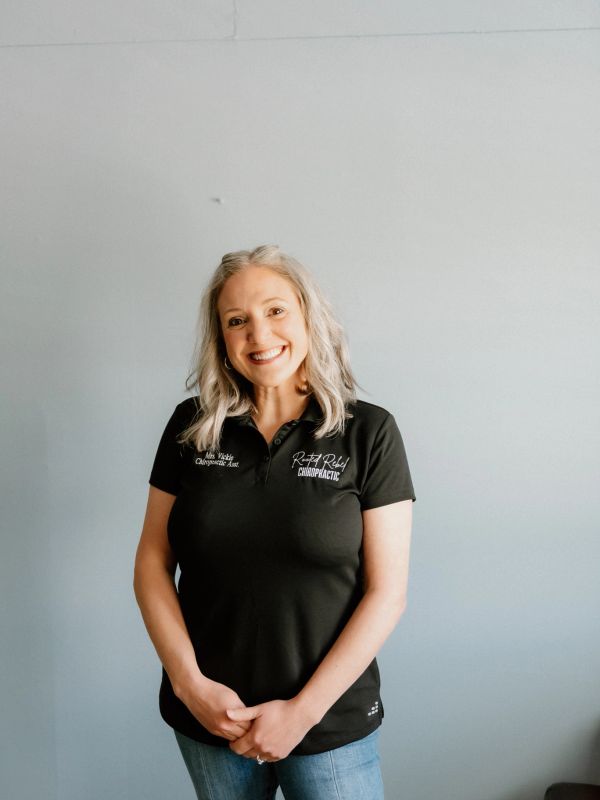 Smiling woman in a black chiropractic assistant polo shirt against a plain background.