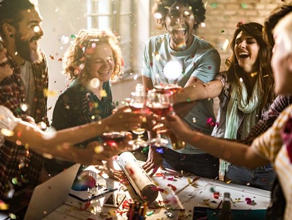 Group of friends toasting with drinks at a lively celebration with confetti.
