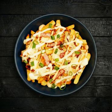 Loaded fries with cheese, bacon, green onions, and creamy sauce in a black bowl.