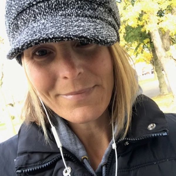 Woman in outdoor attire with a cap and earphones.