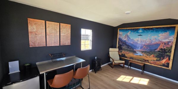 Modern black-walled room with metal table, brown chairs, and colorful mountain mural.