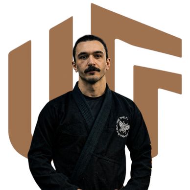 Man in a black martial arts gi holding a brown belt, standing confidently.