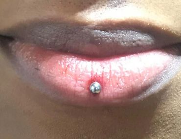 Close-up of lips with a silver lip piercing on the lower lip.