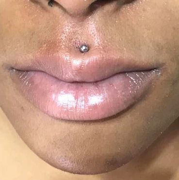 Close-up of lips with a shiny labret piercing above the upper lip.