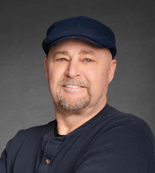 Smiling man in a navy cap and sweater against a gray backdrop.