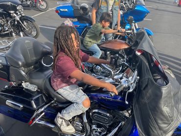 Two boys sitting on parked motorcycles at an outdoor event.