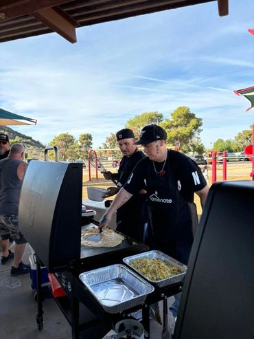 Two men cooking breakfast at an outdoor grill in a park.