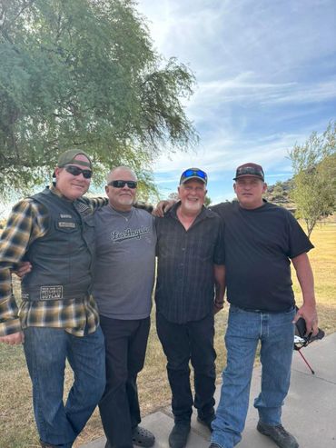 Four men standing together outdoors, smiling and posing for a photo.