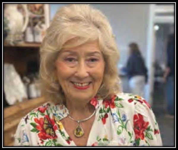 Smiling elderly woman in a floral blouse and pendant necklace.