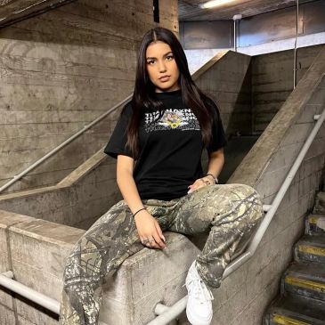 Young woman sitting on a concrete ledge in an industrial setting.