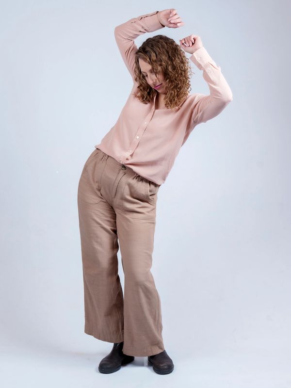 Woman in beige outfit dancing with arms raised against a plain background.