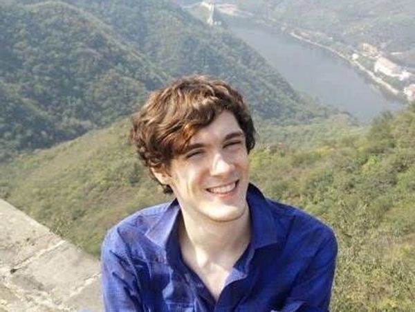 Young man smiling outdoors with river and hills behind.