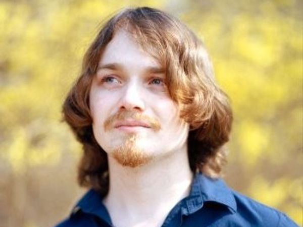 Young man with long hair and a goatee outdoors.