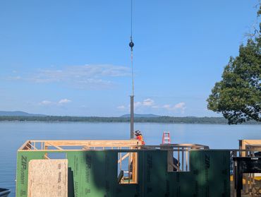 Construction worker assembling wooden structure by a calm lake under clear blue sky.