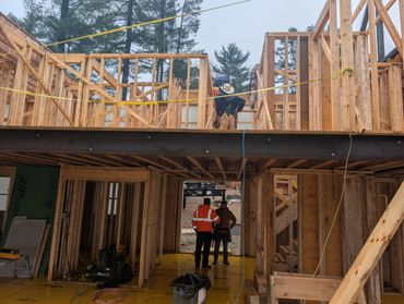 Workers constructing wooden framework of a house under overcast sky.