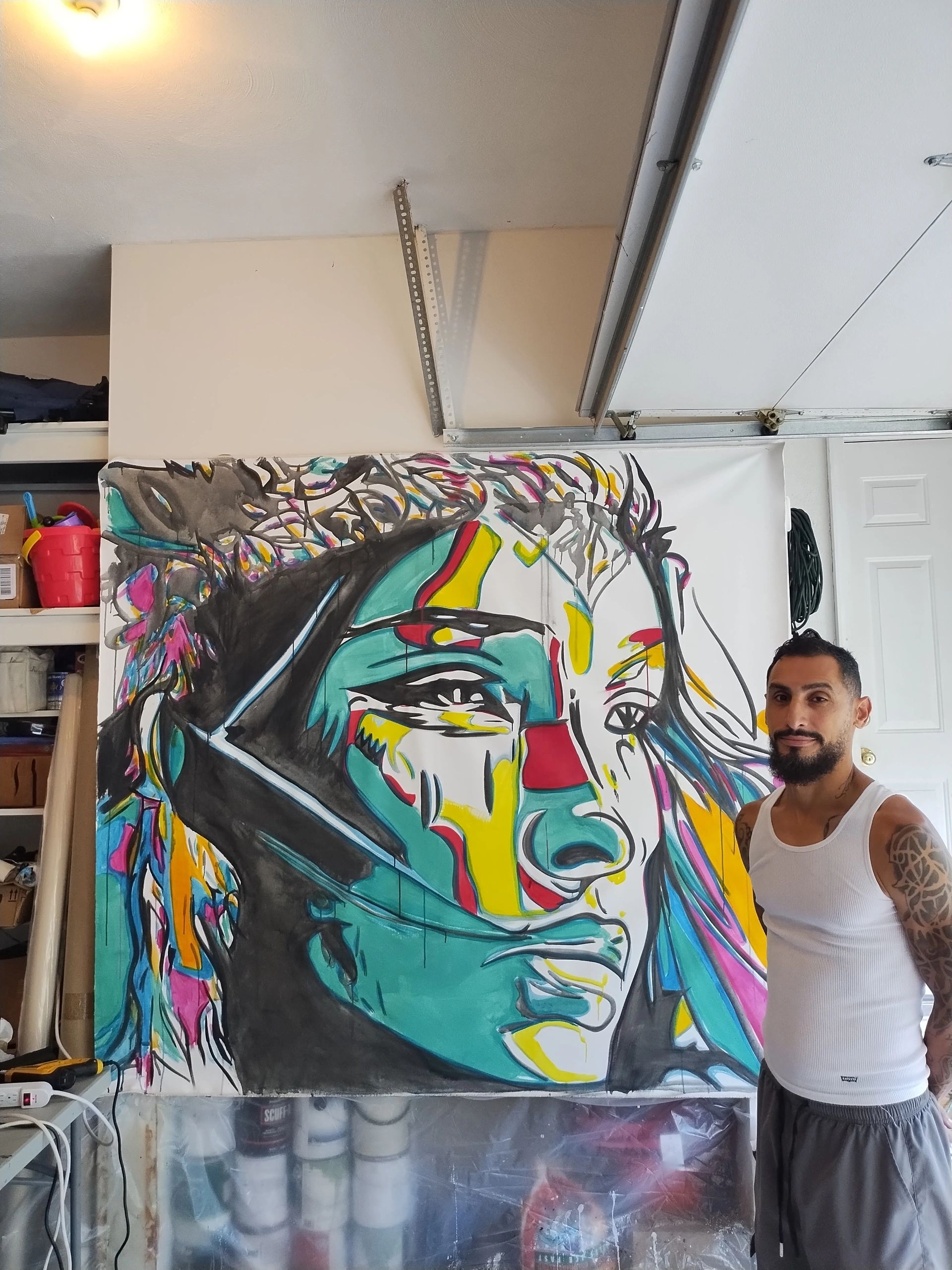 Man posing next to vibrant abstract face painting in a garage.