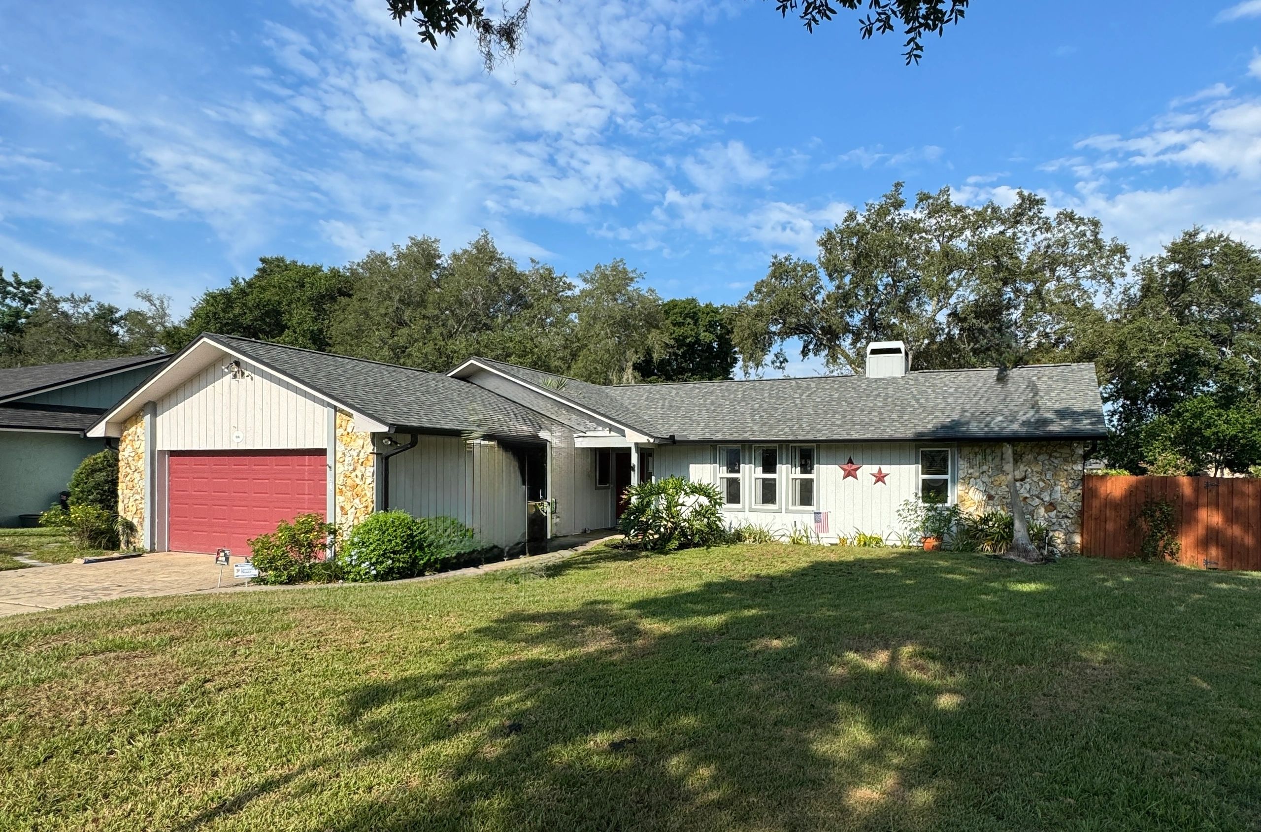 Single-story house with red garage door and large front yard under blue sky.