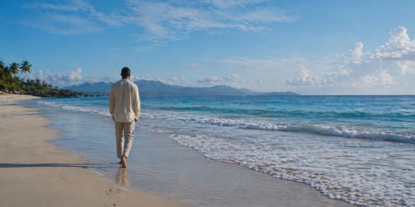 A man walks alone on a sandy beach by the ocean.