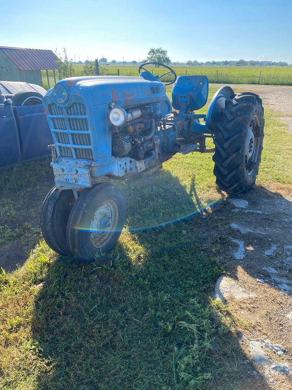 An old blue tractor parked on grass with a rural background.