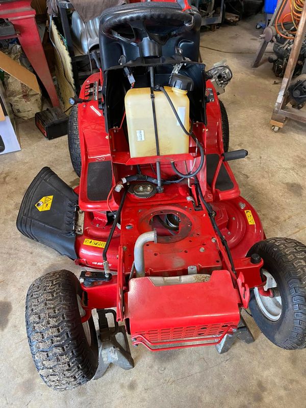 Red riding lawn mower with parts exposed in a garage.