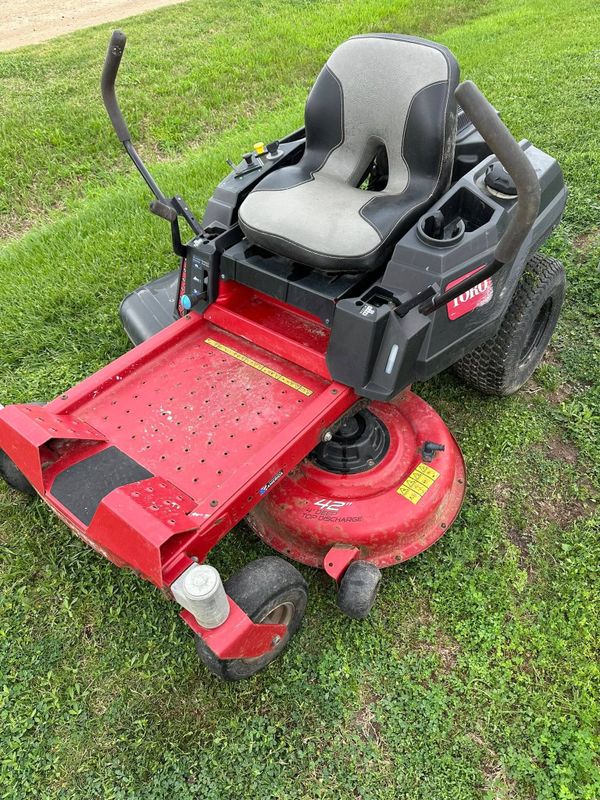 A red riding lawn mower on green grass.