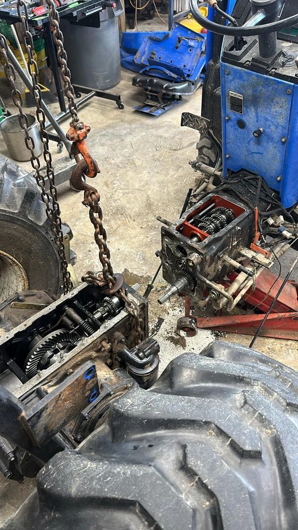 Disassembled tractor gearbox connected by heavy chains in a workshop.