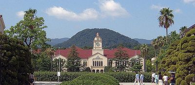 Historic building with a clock tower surrounded by greenery and mountains.