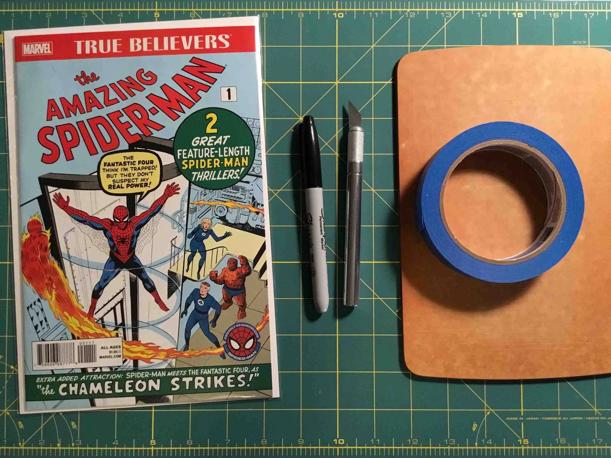 Comic book, pen, craft knife, and tape on a cutting mat.