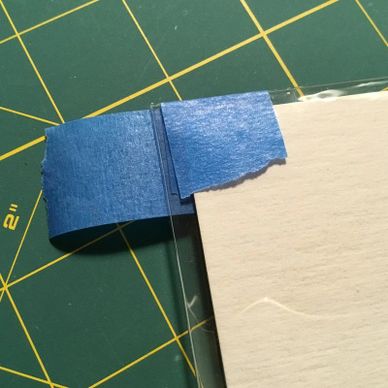 Blue painter's tape holding a transparent sheet over a paper on a cutting mat.