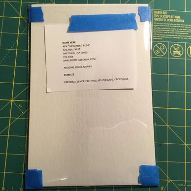 Custom comic book pressing request taped to a board with blue painter's tape.
