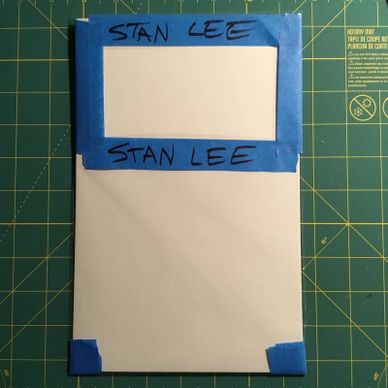 Paper taped with blue painter's tape labeled 'Stan Lee' on a cutting mat.