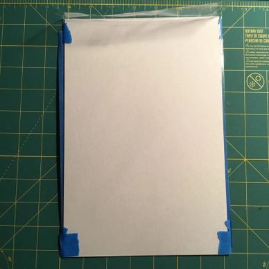 Blank white paper taped on a green cutting mat with measurement markings.