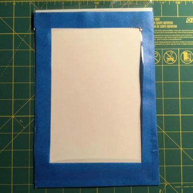 A blank sheet taped to a green cutting mat with blue painter's tape.