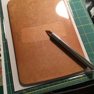 Crafting tools including a precision knife on a cutting mat with a brown cutting board.
